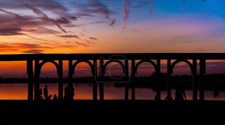 Photo for A sunset scene of a silhouette stone bridge over water for the railway under golden sky - Royalty Free Image