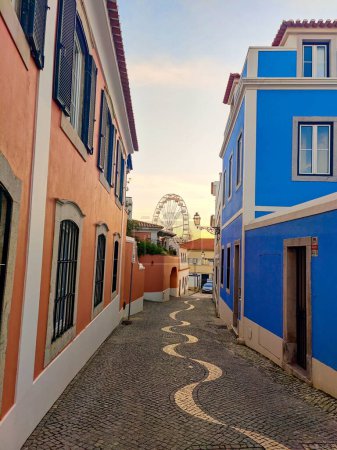 Photo for A narrow cobblestone street between colorful houses to the Ferris wheel on the sunset - Royalty Free Image