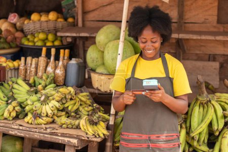 Foto de Una mujer del mercado africano sosteniendo un dispositivo pos y una tarjeta de crédito - Imagen libre de derechos