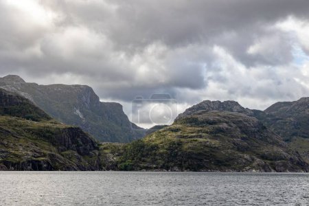 Téléchargez les photos : Une vue panoramique d'immenses montagnes rocheuses dans un ciel nuageux entouré par le lac - en image libre de droit