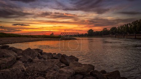 Téléchargez les photos : Un ciel magnifique au coucher du soleil et un paysage nuageux au-dessus d'une rivière avec un pont - en image libre de droit