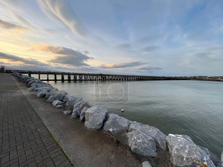 Foto de Una vista panorámica de una costa oceánica con un puente de madera sobre ella en un día soleado - Imagen libre de derechos