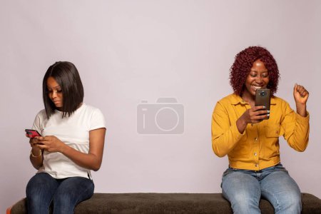 Photo for One girl happy another feels sad while checking their phones - Royalty Free Image
