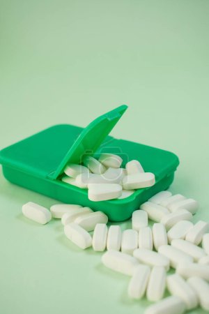 Foto de Un primer plano vertical de pastillas blancas en un pillbox verde sobre un fondo blanco - Imagen libre de derechos
