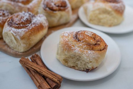 Photo for A closeup of cinnamon buns on white plates with cinnamon sticks near them - Royalty Free Image