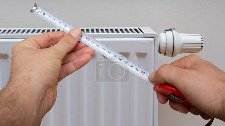 Téléchargez les photos : Une main d'homme tenant une mesure sur un radiateur blanc moderne - en image libre de droit