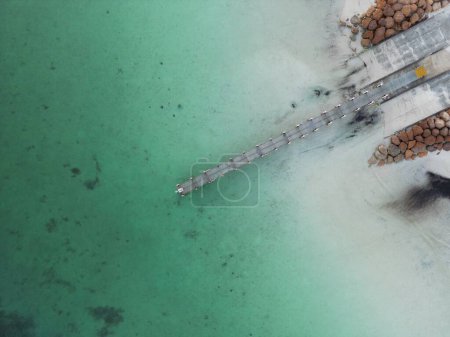 Téléchargez les photos : Une vue aérienne d'une jetée entourée d'eau de mer avec une côte rocheuse en plein jour - en image libre de droit