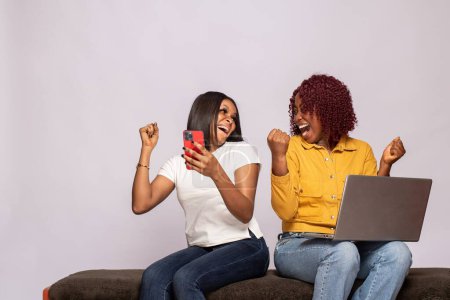 Photo for Two black girls using their phone and laptop rejoice - Royalty Free Image