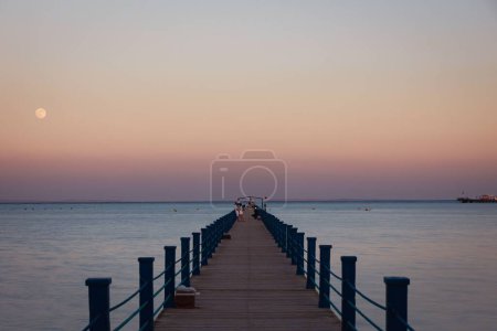 Foto de Un mar tranquilo y un muelle de madera contra el cielo rosado del atardecer con luna llena - Imagen libre de derechos