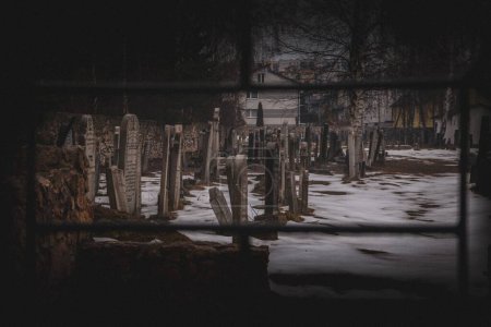 Foto de Una escena de un cementerio visto entre rejas con el suelo cubierto de nieve y árboles desnudos durante el día - Imagen libre de derechos