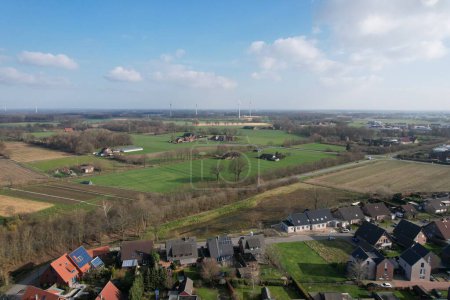Téléchargez les photos : Vue aérienne d'un village avec des maisons entourées d'un champ herbeux sous le ciel bleu ensoleillé - en image libre de droit