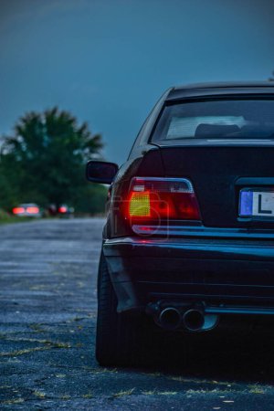 Photo for A vertical shot of the back of the car with the illuminated brake light on the blurred background - Royalty Free Image