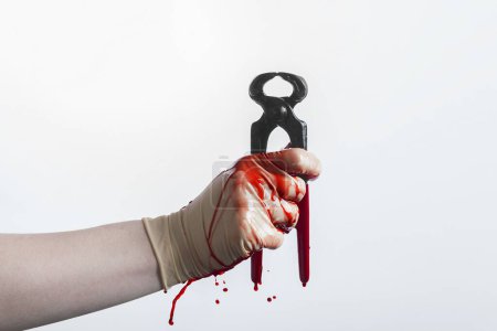 Foto de La sangre goteando sobre alicates y un guante de plástico frente a un fondo blanco. - Imagen libre de derechos