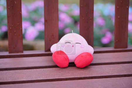 Foto de Un primer plano de un animal de peluche rosa San-ei Kirby Sleeping Mascot en un banco de madera - Imagen libre de derechos