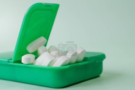 Foto de Un primer plano de píldoras blancas en un pillbox verde sobre un fondo blanco - Imagen libre de derechos