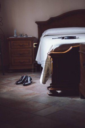 Téléchargez les photos : Un plan vertical d'une paire de chaussures masculines noires sur le sol et une ceinture sur le lit - en image libre de droit