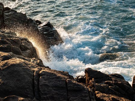 Téléchargez les photos : Les vagues mousseuses de la mer frappant les gros rochers sur le rivage pendant la journée - en image libre de droit