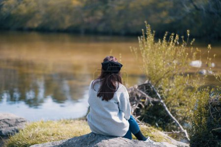 Téléchargez les photos : Une vue panoramique d'une femme assise sur un rocher au bord de la rivière par une journée ensoleillée - en image libre de droit
