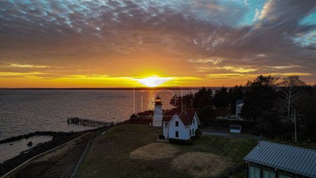 Téléchargez les photos : Un coup de drone de splendide coucher de soleil sur la mer et un phare à côté d'une maison sur le rivage - en image libre de droit