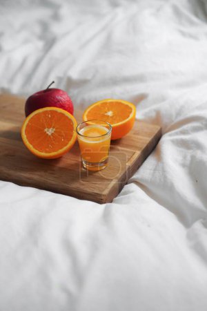 Foto de Un primer plano de naranja cortada con un vaso de jugo de naranja y manzana a bordo en la cama blanca - Imagen libre de derechos