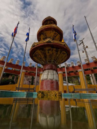 Photo for A low-angle shot of a Fountain in Jocotan downtown in Guatemala, with flags and cloudy sky in the background - Royalty Free Image