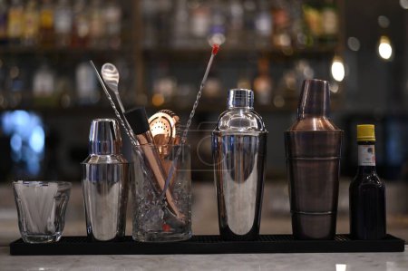 Foto de Un primer plano del conjunto de accesorios de bar para hacer cócteles alineados uno junto al otro contra un estante lleno de bebidas alcohólicas fuertes - Imagen libre de derechos