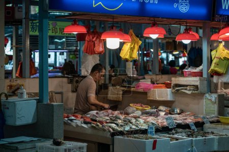 Foto de Un hombre vendiendo pescado en el mercado húmedo de Whampoa con luces colgantes - Imagen libre de derechos