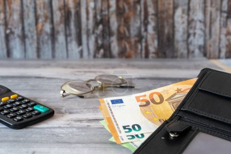 Téléchargez les photos : Un gros plan de billets en euros sur un portefeuille et des lunettes près d'un ordinateur portable - en image libre de droit