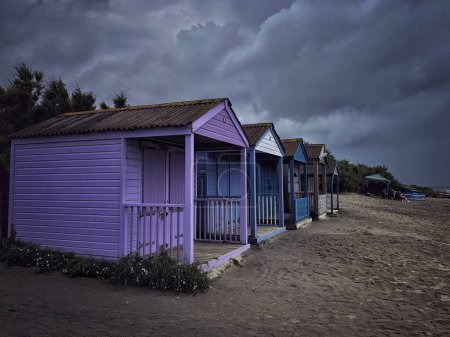 Téléchargez les photos : Un groupe de petites cabanes près de la plage par une journée nuageuse - en image libre de droit