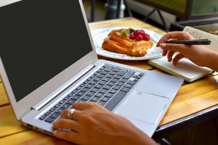 Photo for A closeup shot of a young female working on her laptop and having a croissant in a cafe - Royalty Free Image