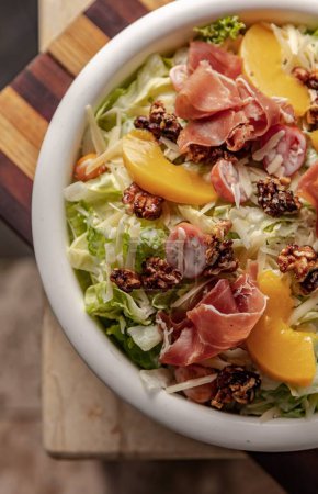 Photo for A vertical top view of a gourmet mixed salad with lettuce, peaches, tomatoes, walnuts, and prosciutto - Royalty Free Image