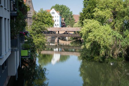 Téléchargez les photos : Un pont, des arbres et des bâtiments reflétés sur la rivière Pegnitz par une journée ensoleillée - en image libre de droit