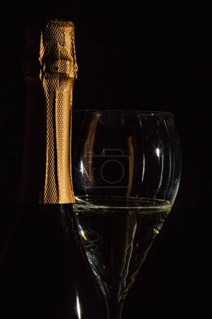 Photo for A glass of sparkling wine beside a champagne bottle isolated on a black background - Royalty Free Image