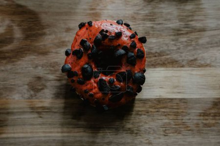 Foto de Un primer plano de un donut recién horneado, glaseado con chocolate y decorado con chispas de chocolate, sobre un fondo de madera - Imagen libre de derechos