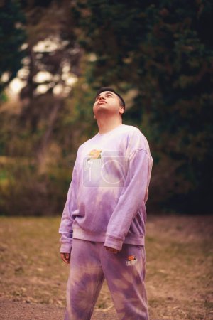 Photo for A vertical shot of a young Hispanic man in a purple tie-dye sports costume in a park - Royalty Free Image