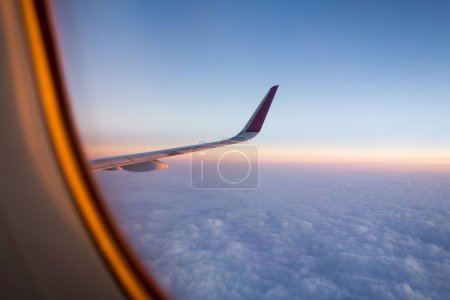 Téléchargez les photos : Plan rapproché de l'aile d'un avion depuis un siège côté allée et du ciel au coucher du soleil - en image libre de droit