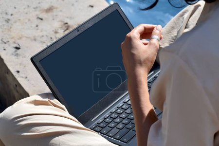 Foto de Un primer plano de una joven mujer trabajando en su portátil con una pantalla en blanco en un parque - Imagen libre de derechos