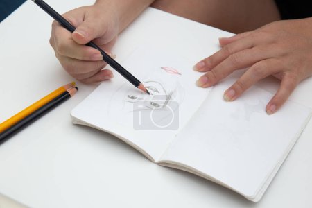 A closeup shot of a female hand drawing and sketching a face in a notebook-stock-photo