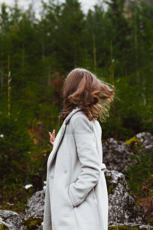 Photo for A vertical shot of a young Caucasian female walking in a forest wearing a white coat - Royalty Free Image