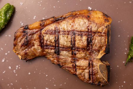 Photo for A close-up shot of grilled T-bone steak with chilis served with brown plate in restaurant - Royalty Free Image