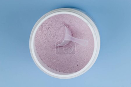 Téléchargez les photos : Une poudre de protéines rose avec cuillère en fond bleu - en image libre de droit