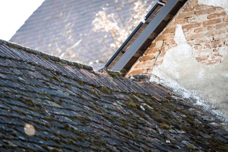 Téléchargez les photos : Un vieux toit de tuiles de mousse sur une vieille maison de briques sous un soleil éclatant - en image libre de droit