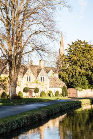 Photo for A row of historic quintessential Cotswold cottages by a river in Cotswolds, England, vertical shot - Royalty Free Image