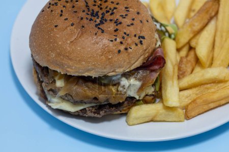 Téléchargez les photos : Gros plan d'un cheeseburger avec des frites sur une assiette blanche sur une table bleu clair - en image libre de droit