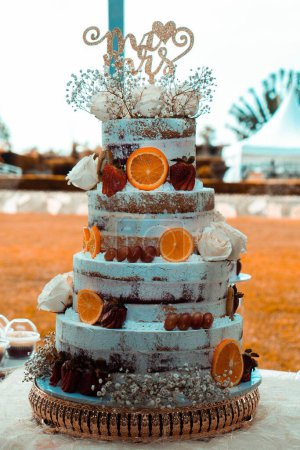 Téléchargez les photos : Un gros plan vertical d'un gâteau de mariage à 4 niveaux décoré de fruits frais et de roses blanches - en image libre de droit