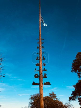 Téléchargez les photos : Plan vertical d'un Maibaum (Maypole) décoré, surmonté d'un drapeau, érigé par une journée ensoleillée - en image libre de droit