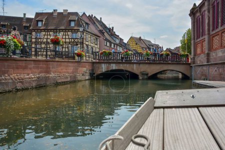 Foto de Una vista mientras navega por el canal en el centro de la ciudad de Colmar mostrando un pequeño puente sobre el agua y hermosas arquitecturas en Francia - Imagen libre de derechos