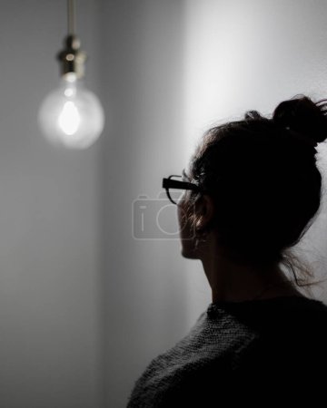 Téléchargez les photos : Un plan vertical d'une femme caucasienne avec ses cheveux lapidés, portant des lunettes, et regardant une lampe allumée - en image libre de droit