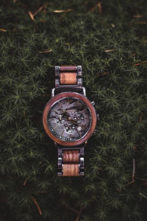 Foto de Un primer plano de un hermoso reloj de madera de nogal sobre un fondo verde oscuro de hojas - Imagen libre de derechos