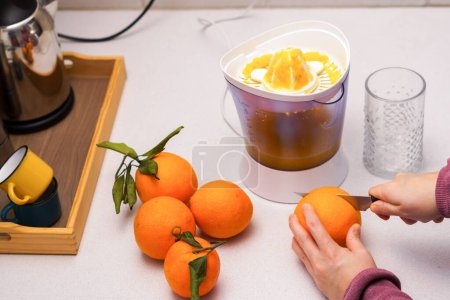 Photo for Woman's hands cutting an orange with a knife to make juice with the juicer in the background - Royalty Free Image